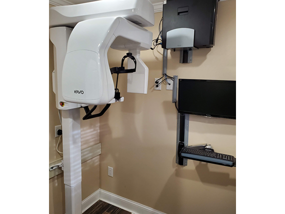 The image shows a medical dental office with equipment, including a large overhead light with a movable arm, and a computer monitor on the wall.