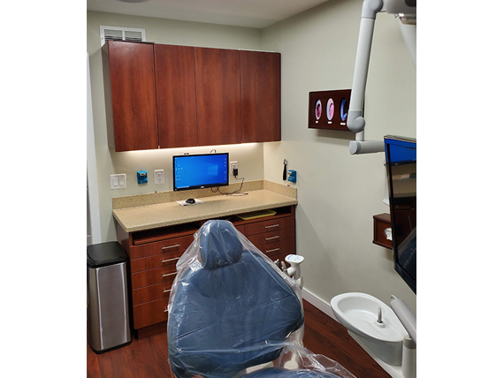 Alt text   A dental office with a modern chair, desk, computer monitor, and a covered patient chair.