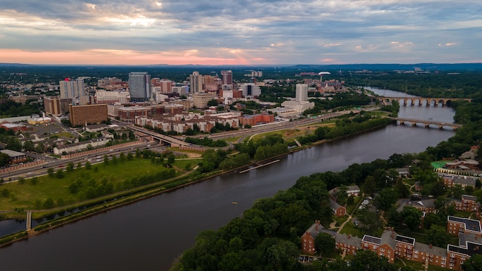 Aerial view of a cityscape at sunset with a river running through the center, featuring a bridge and a skyline.