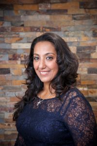 The image features a woman standing in front of a brick wall, smiling at the camera.