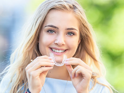 A young woman with a radiant smile, holding up a toothbrush with her mouth.