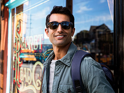 Man in sunglasses, standing outdoors with a backpack, smiling at the camera.