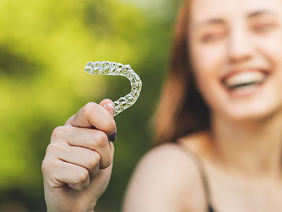 A person holding a toothbrush with bristles, smiling and standing outdoors.