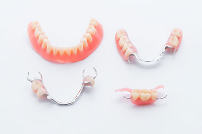 The image shows a collection of dentures with artificial teeth, displayed on a white background against a gray gradient.