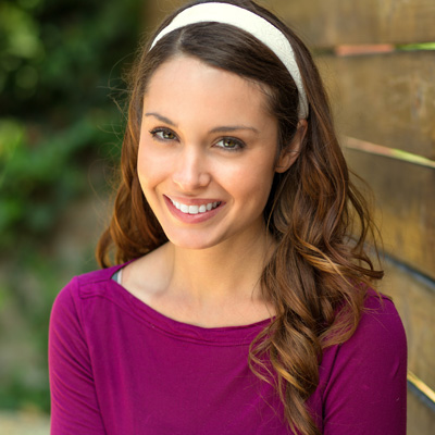 The image shows a woman with long hair, wearing a purple top and a headband, smiling at the camera.