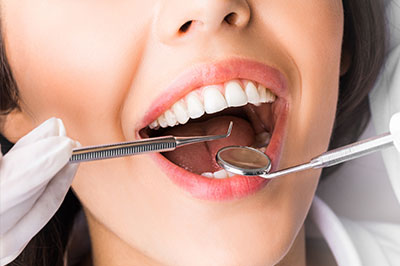 A woman undergoing dental care, with a toothbrush in her mouth and a dental mirror held up to her teeth by a person wearing gloves.