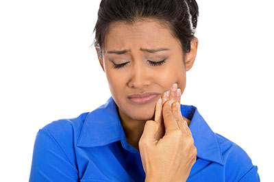 A woman with a concerned expression, holding her face and possibly brushing her teeth, against a plain background.