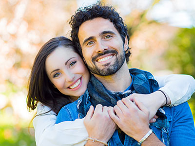 A man and woman are embracing each other in a joyful pose, with the man wearing a scarf around his neck.