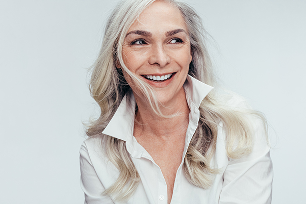 The image shows a woman with blonde hair, wearing a white shirt and smiling at the camera.