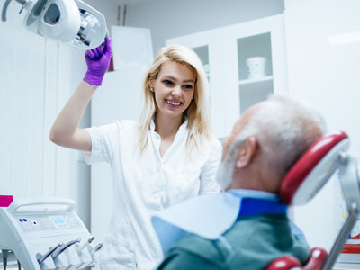 A dental professional assisting a patient with dental equipment.