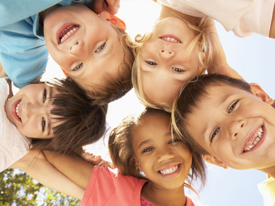 A group of smiling children in a sunny outdoor setting, posing for the camera.