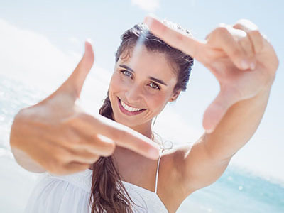 A woman is taking a selfie with her hand, smiling at the camera.