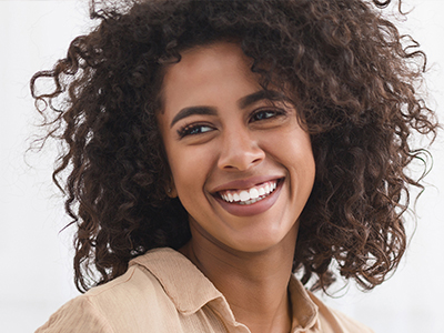 The image shows a smiling woman with curly hair, wearing a light-colored top, against a white background.